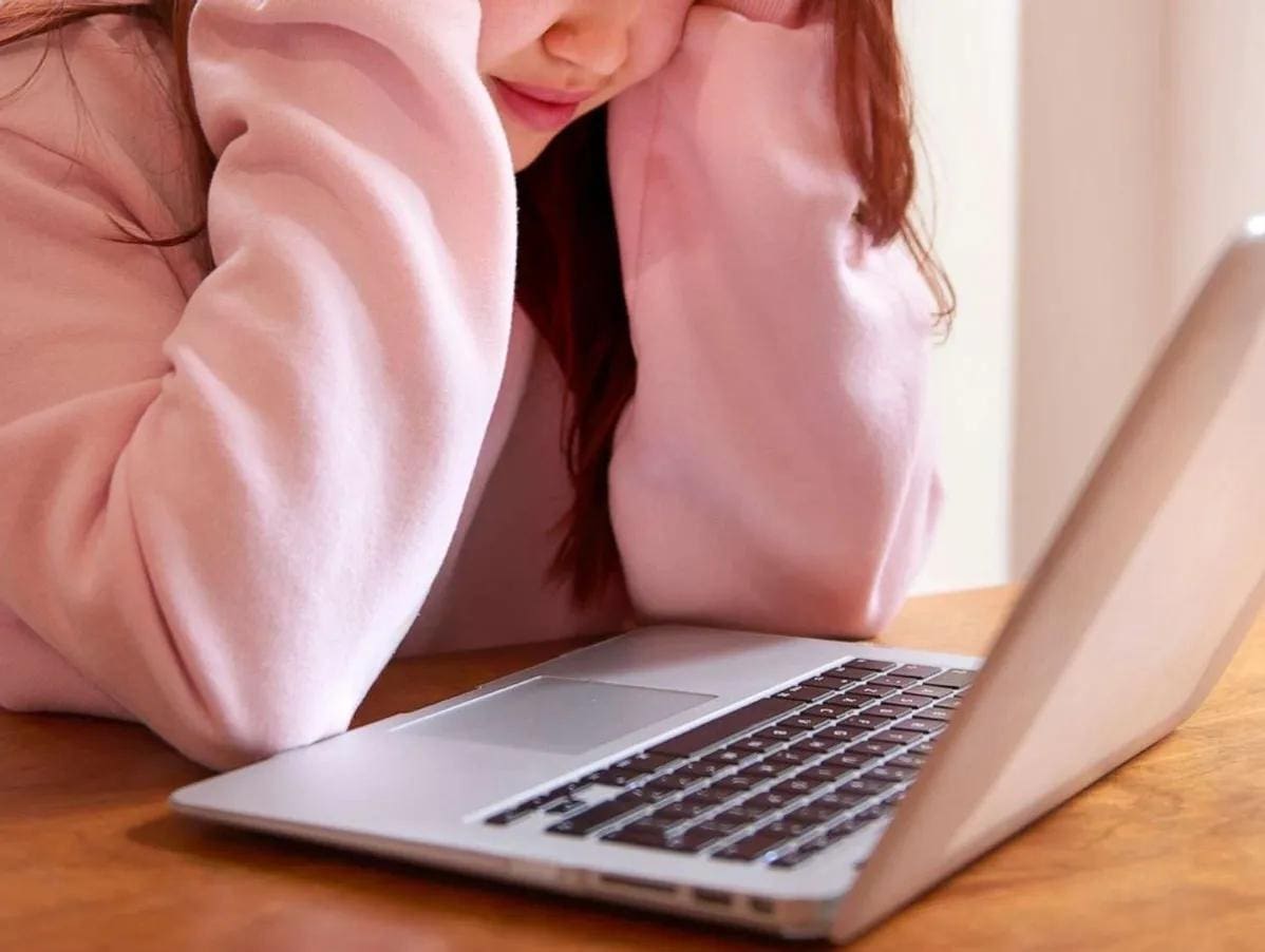 1745322389989_IMAGE-52725_20_283_29 A woman in a pink sweater gazes intently at her laptop screen, focused on her work or browsing online.
